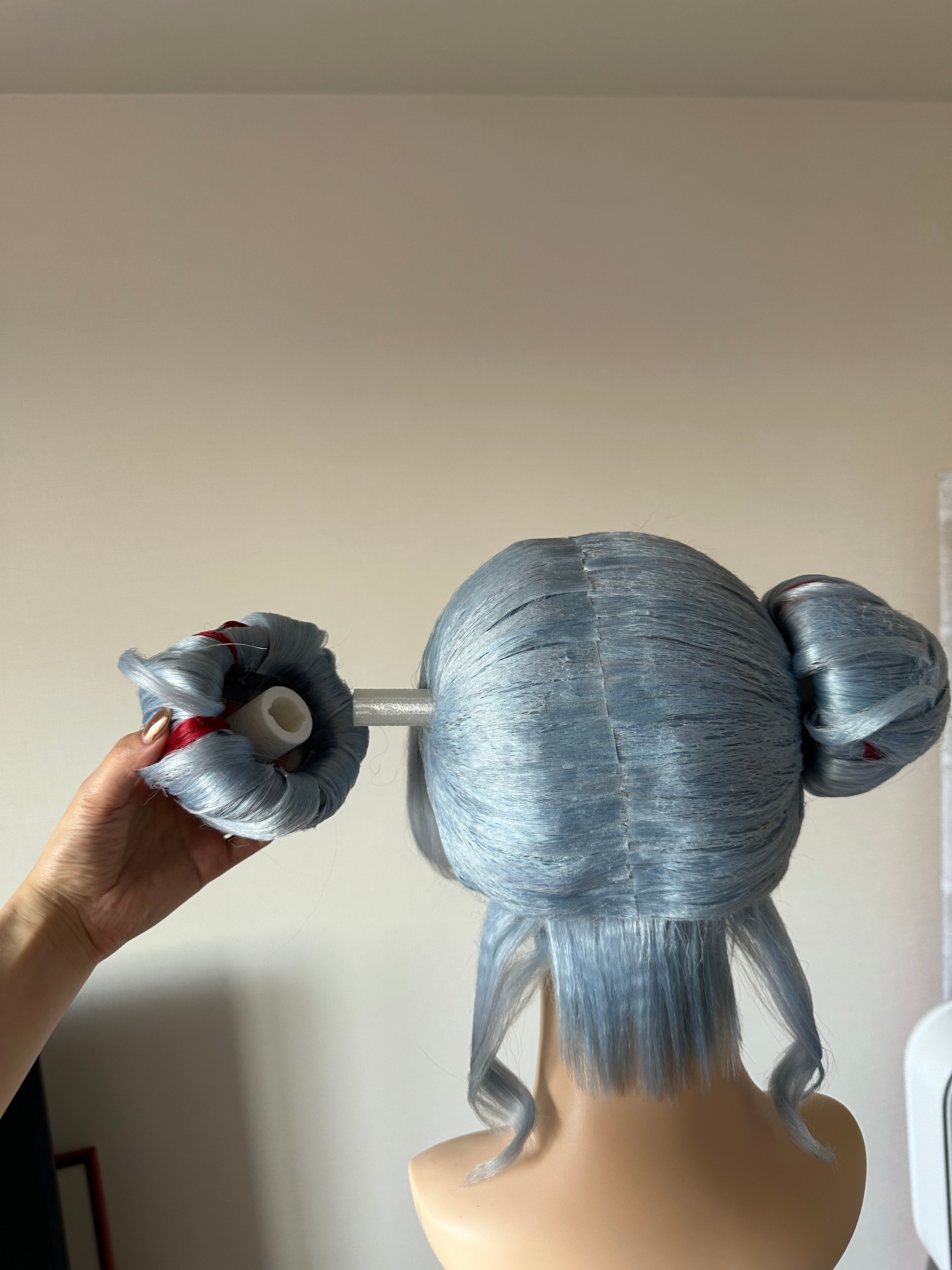 A silver-blue wig with two buns being shaped by hand on a mannequin head during production