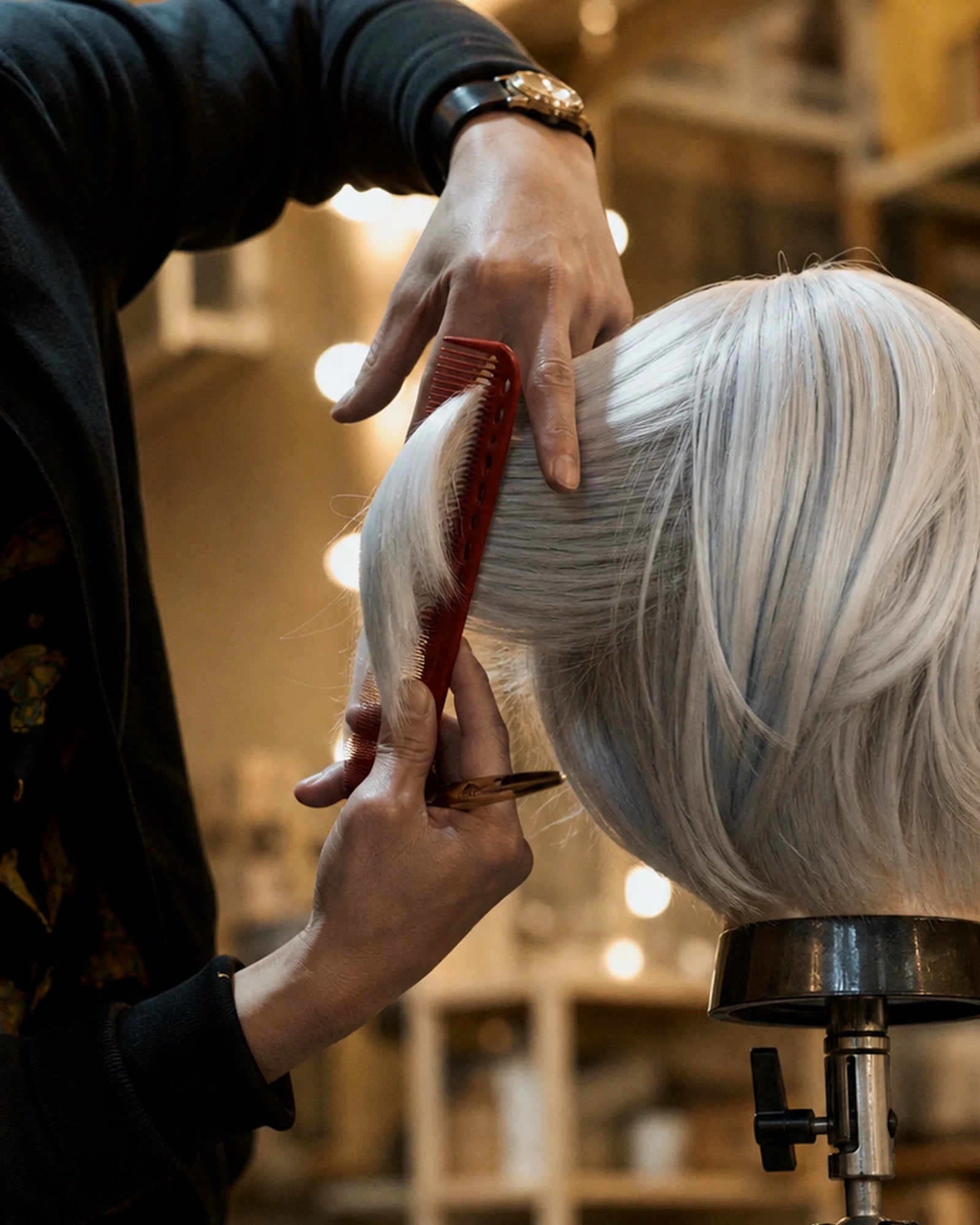 A stylist working by hand on a silver wig mounted on a stand
