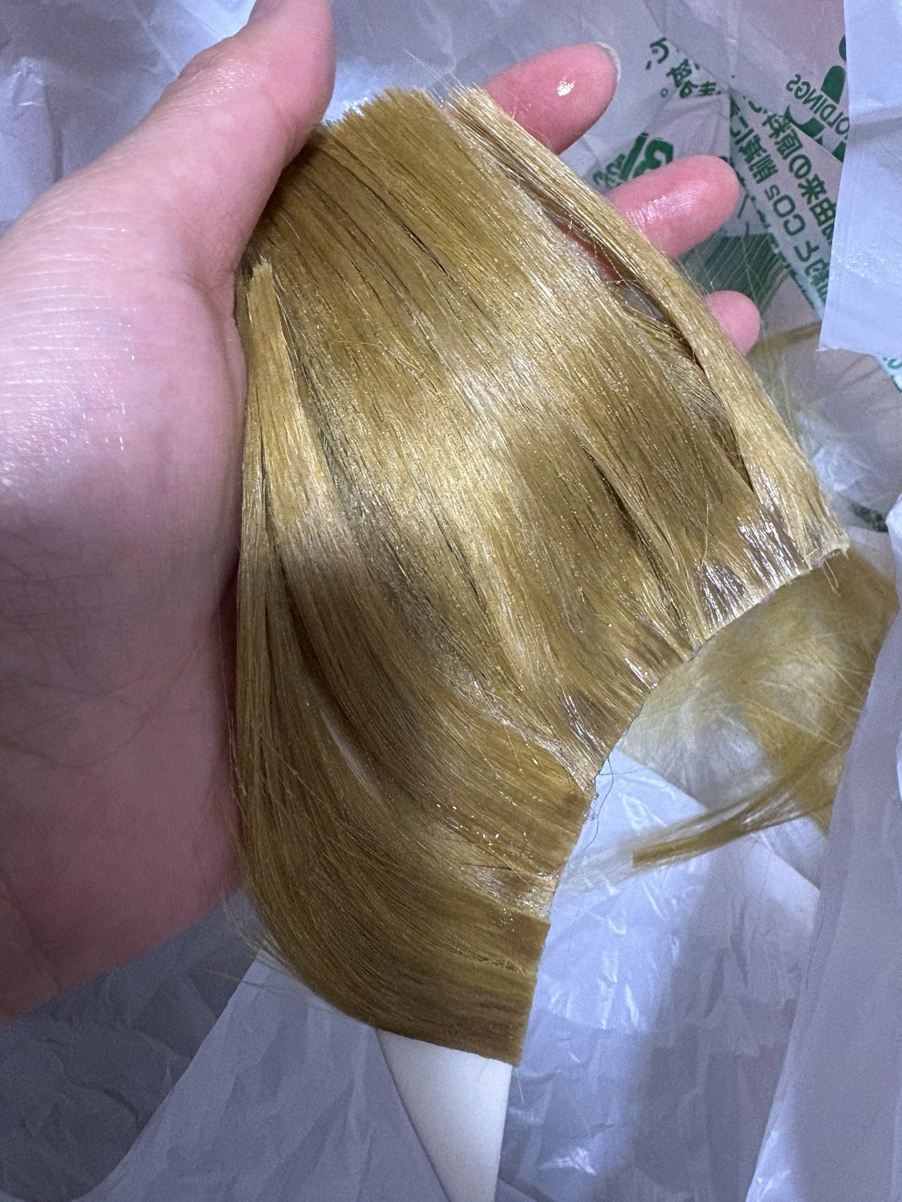 A finished wig wrapped in protective material, held in one hand before packing