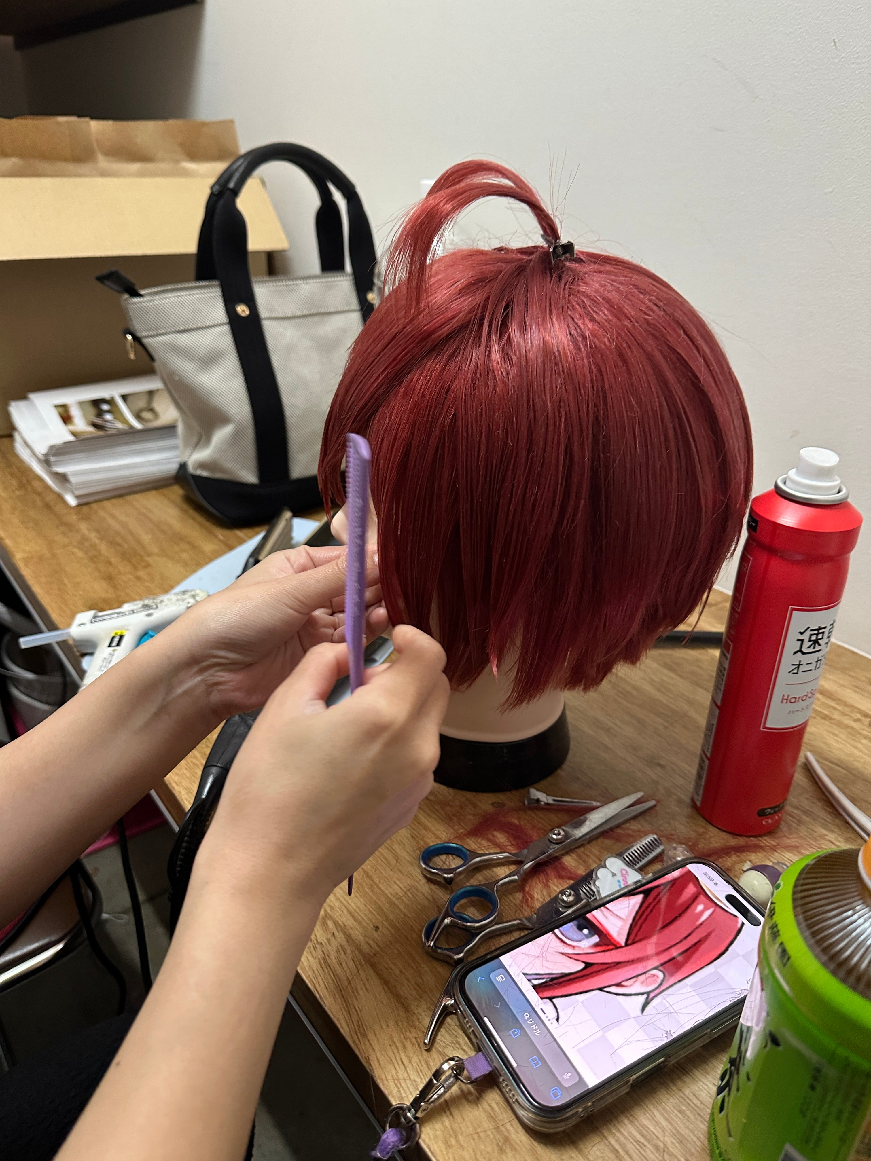 Wig artist shaping a red wig while checking the character reference on a phone
