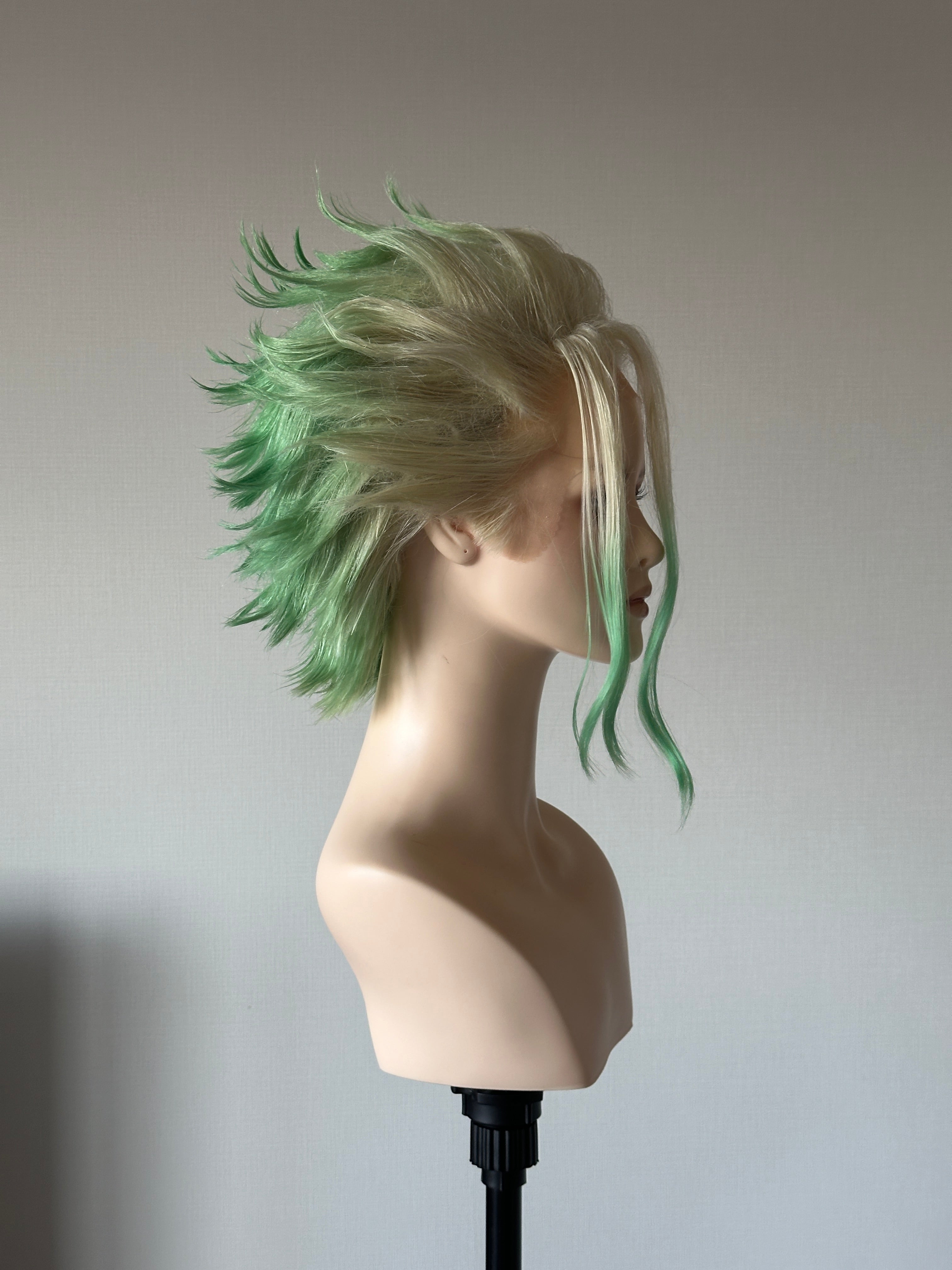 A finished green and blonde wig on a display bust, photographed from the side for review