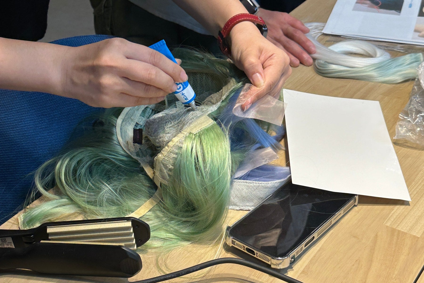 Several hands working together on a green wig at one workbench